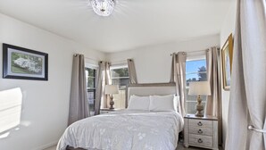 Une chambre à coucher avec un lit, des tables de chevet, des rideaux, un lustre et un tableau encadré au mur.
