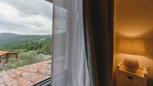 A room with a view of a mountainous landscape through a window with curtains. There is a bedside table with a lamp and a decorative vase. - Le Fonti - Molino, chic and reserved (Pontassieve)