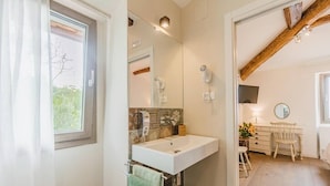 A bathroom with a sink, mirror, and towel rack. There is a window with curtains, a wooden ceiling beam, and a small trash bin. - Le Fonti - Molino, chic and reserved (Pontassieve)