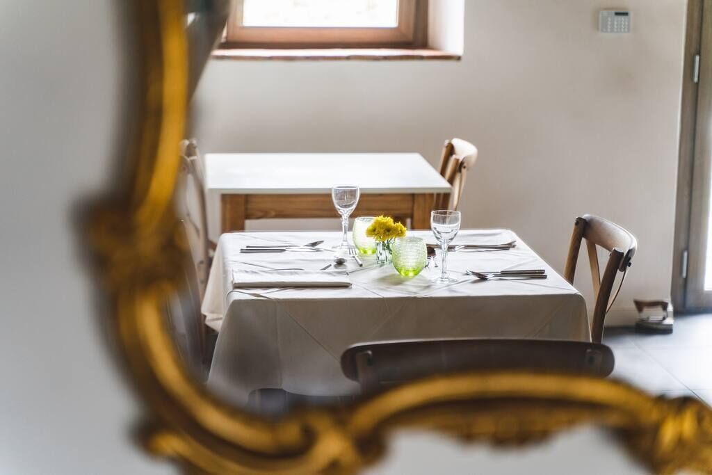 A dining table set with a white tablecloth, two wine glasses, a vase with yellow flowers, and a small bowl.