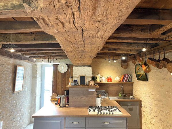 A rustic kitchen with exposed wooden beams, a gas stove, and hanging pots.