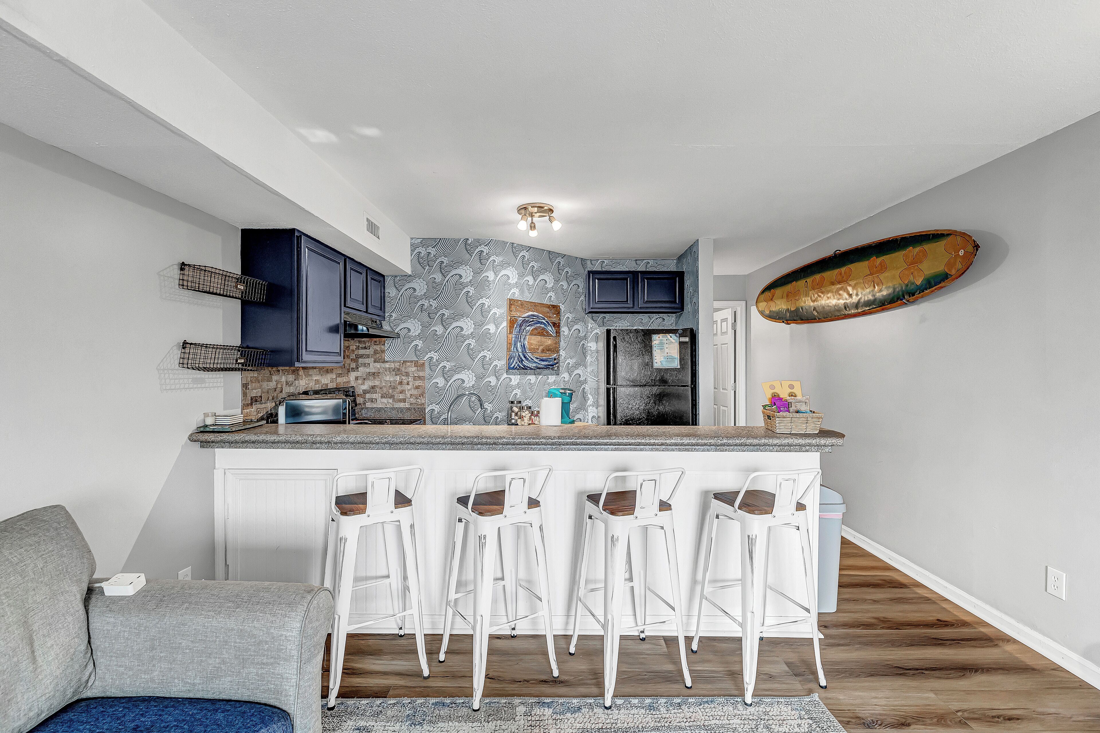 A modern kitchen with a central island, bar stools, and a surfboard on the wall.