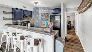 A modern kitchen with a central island, bar stools, and a backsplash with a wave pattern. - Coastal Cozy Condo: Pet Friendly! Steps to Beach, Perfect for Relaxing Getaways! (Carolina Beach)