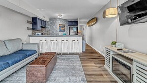 A modern kitchen with a central island, bar stools, and a dining area with a sofa and a coffee table. - Coastal Cozy Condo: Pet Friendly! Steps to Beach, Perfect for Relaxing Getaways! (Carolina Beach)