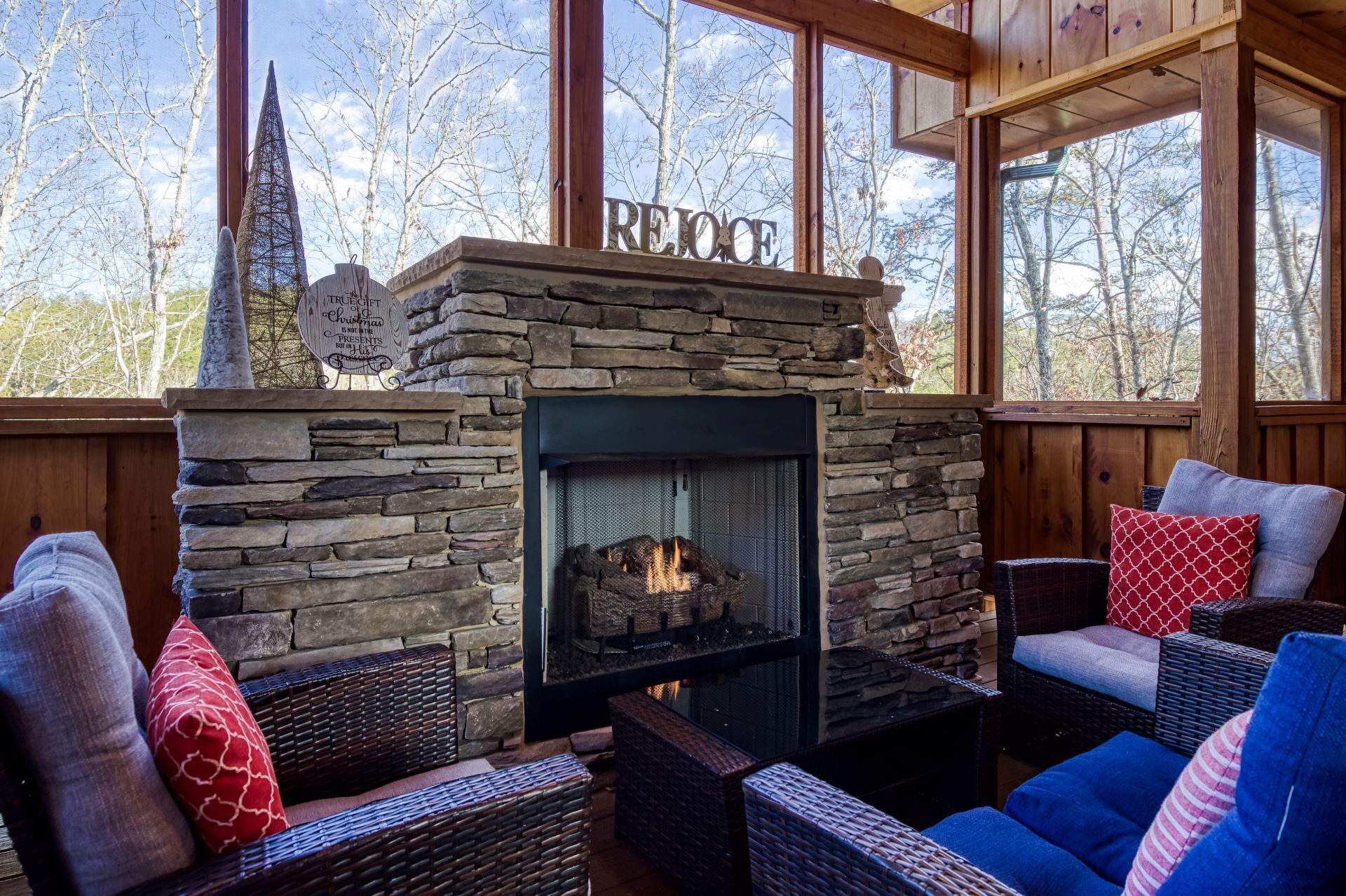 A cozy fireplace area with stone walls, wicker furniture, and a 'REJOICE' sign above the fireplace.