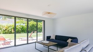 Ett modernt vardagsrum med en soffa, ett soffbord och en stor skjutdörr i glas som leder ut till ett utomhusområde med en gräsmatta och trädgårdsmöbler.
