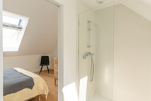 Une chambre à coucher comprenant un lit, une chaise, une commode et une cabine de douche en verre.