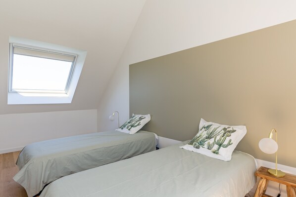 Une chambre avec deux lits, une lucarne, une lampe de chevet et un coussin décoré de motifs de cactus.