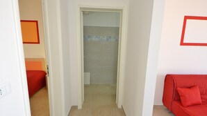 A hallway with a red couch, a door leading to a bathroom, and a tiled floor.