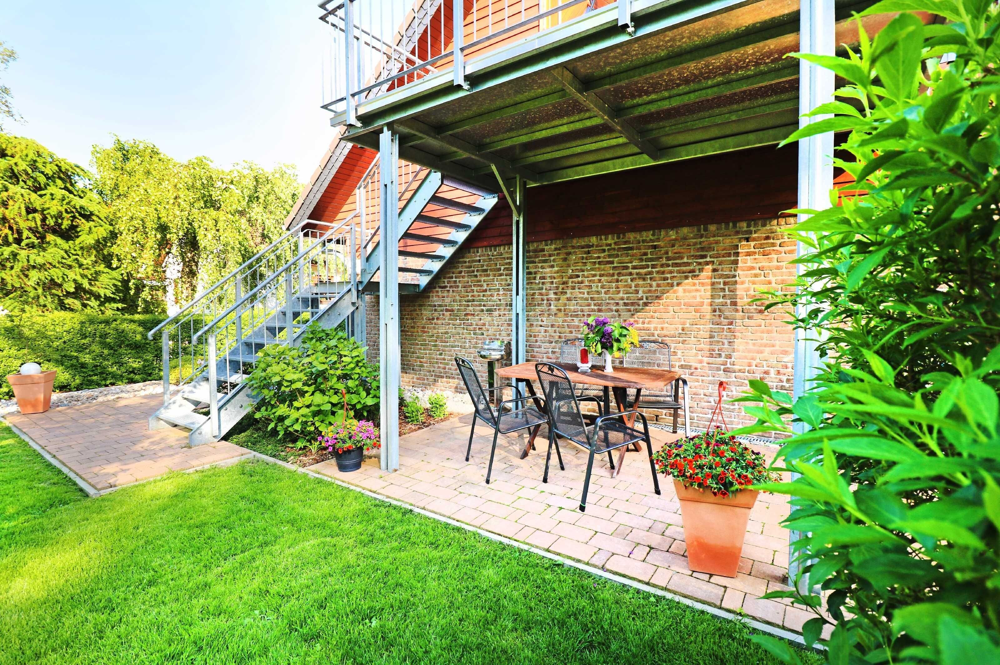 Eine Terrasse mit Ziegelmauer, einer Metalltreppe und einem Tisch mit Stühlen.