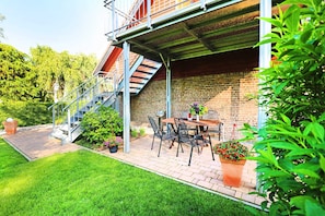 Un patio con un muro de ladrillo, una escalera de metal y una mesa con sillas.