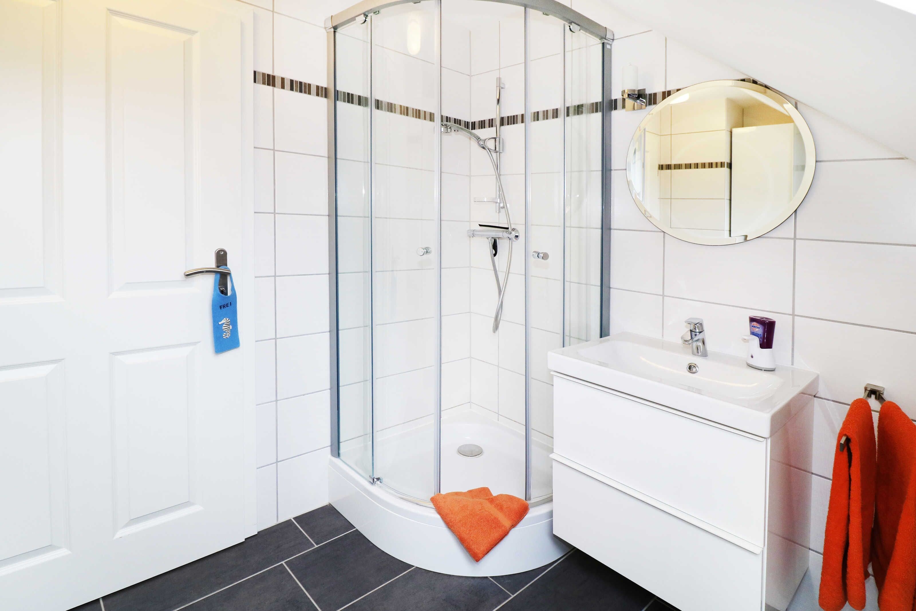 Ein modernes Badezimmer mit einer Duschkabine aus Glas, einem weißen Waschbecken und einem Spiegel.