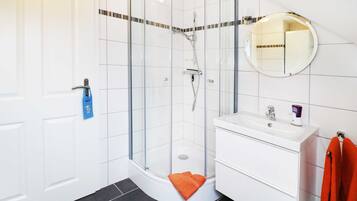 Ein modernes Badezimmer mit einer Duschkabine aus Glas, einem weißen Waschbecken und einem Spiegel.