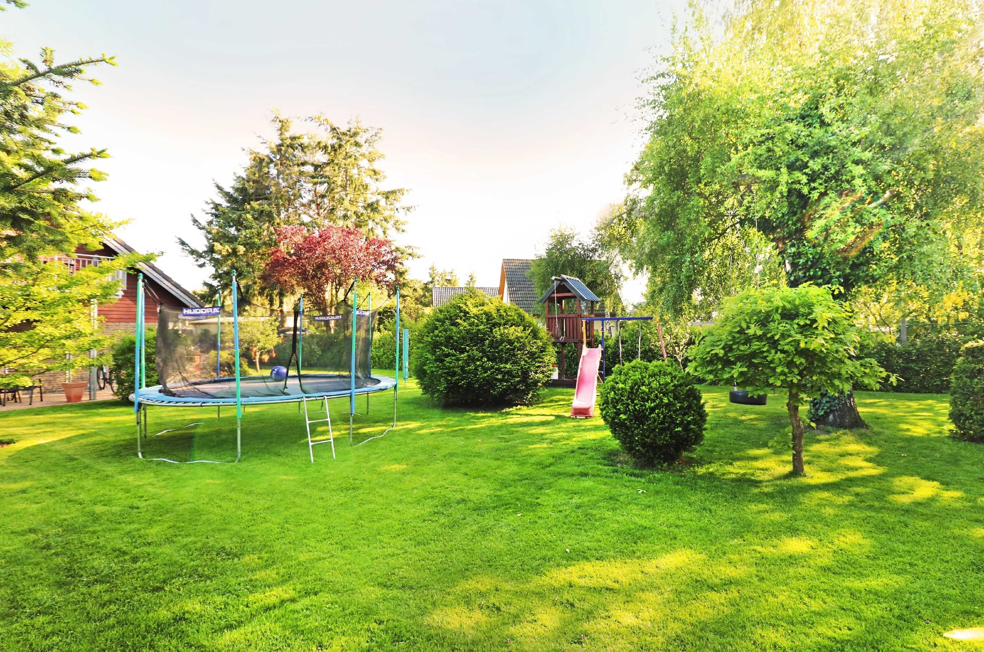 Ein gepflegter Garten mit Trampolin, Rutsche sowie verschiedenen Bäumen und Büschen.
