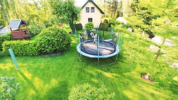 Ein Trampolin in einem gepflegten Garten, im Hintergrund ein Haus.