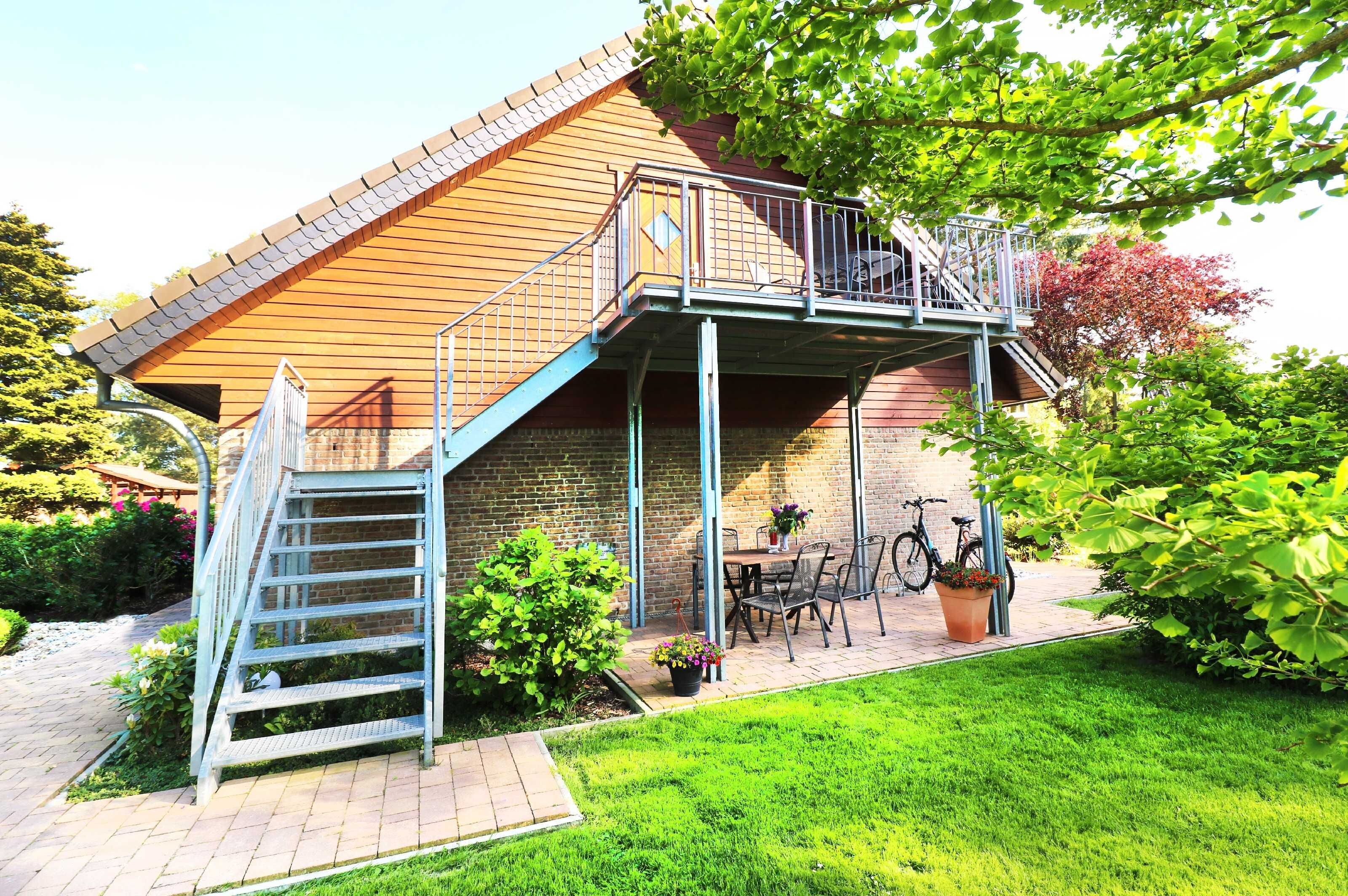 Ein zweigeschossiges Haus mit einem Balkon, einer Treppe, einer Terrasse mit Tisch und Stühlen sowie einem Fahrrad.