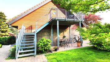 Ein zweigeschossiges Haus mit einem Balkon, einer Treppe, einer Terrasse mit Tisch und Stühlen sowie einem Fahrrad.