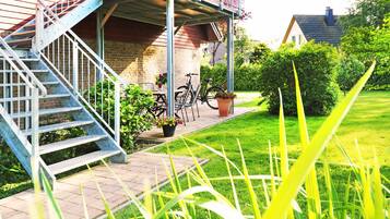 Ein Wohngebäude mit überdachter Veranda, einer Treppe und einem Garten mit Rasen und Pflanzen.