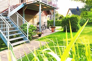 A residential building with a covered porch, a staircase, and a garden area with grass and plants. - Wolfgram Apartment with Balcony - Ferienwohnung Wolfgram (Trassenheide)