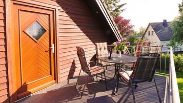 Eine Holzterrasse mit Tisch und Stühlen, eine Tür mit einem rautenförmigen Fenster und ein Blick auf ein Haus im Hintergrund.