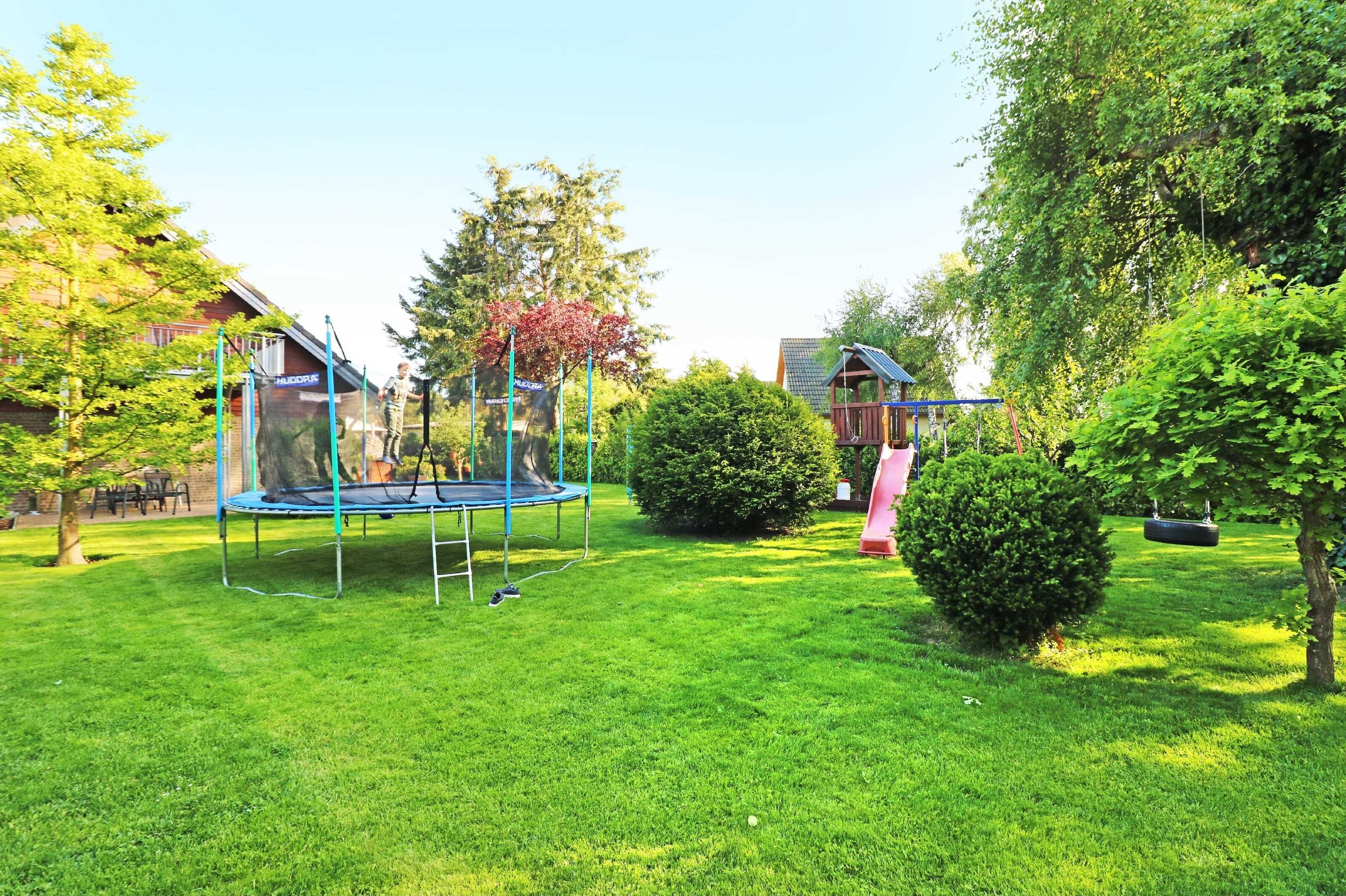 Ein grünes Hinterhof mit Trampolin, Schaukel und einer kleinen Gartenhütte.