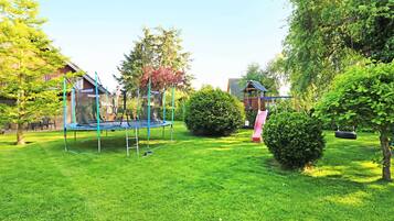 Ein grünes Hinterhof mit Trampolin, Schaukel und einer kleinen Gartenhütte.