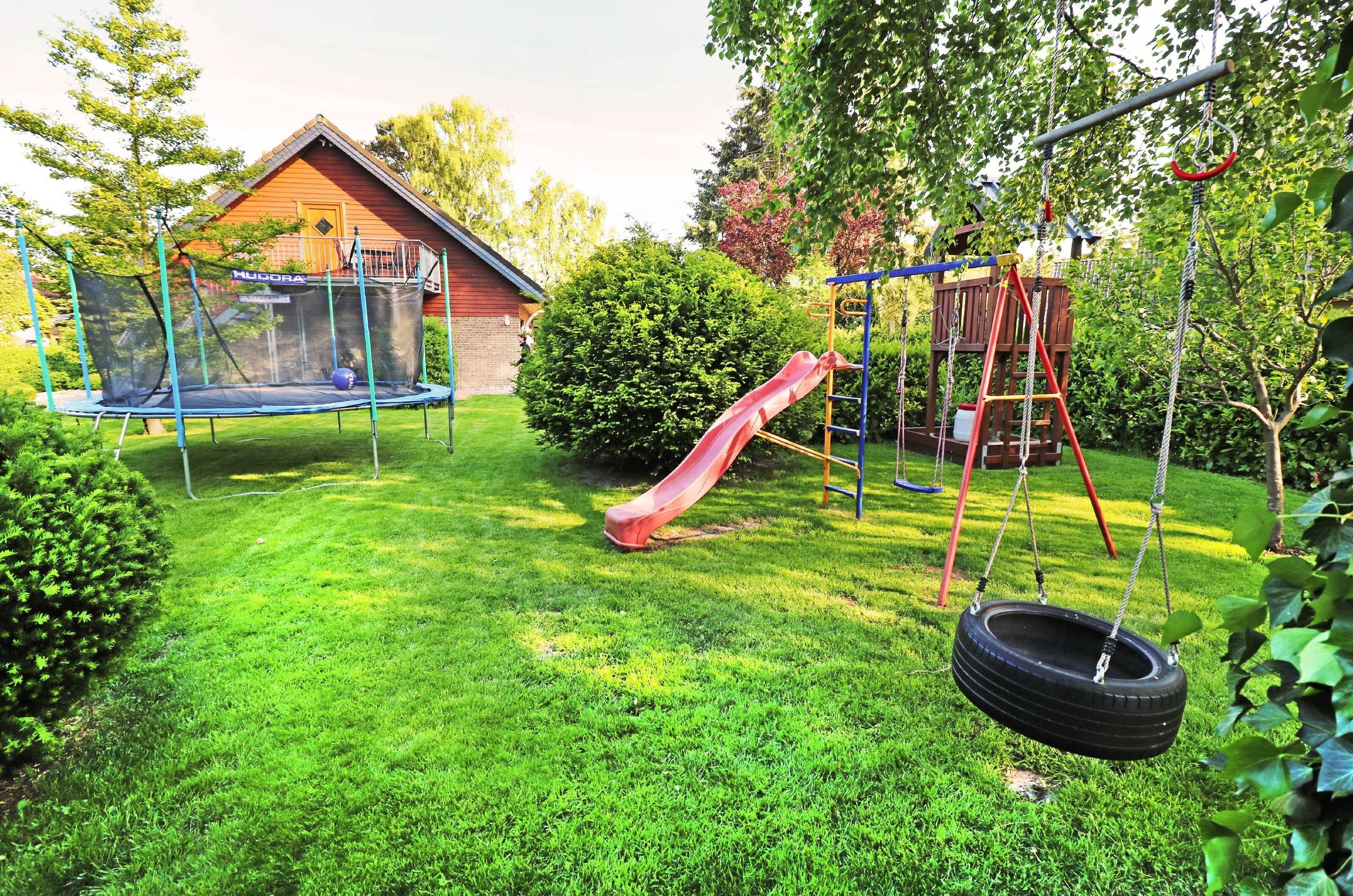 Ein Garten mit Trampolin, einer Taitschaukel, einer Rutsche und einer Schaukel.