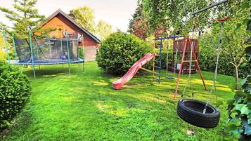 Ein Garten mit Trampolin, einer Taitschaukel, einer Rutsche und einer Schaukel.