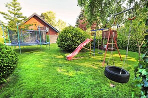 Ein Garten mit Trampolin, einer Taitschaukel, einer Rutsche und einer Schaukel.