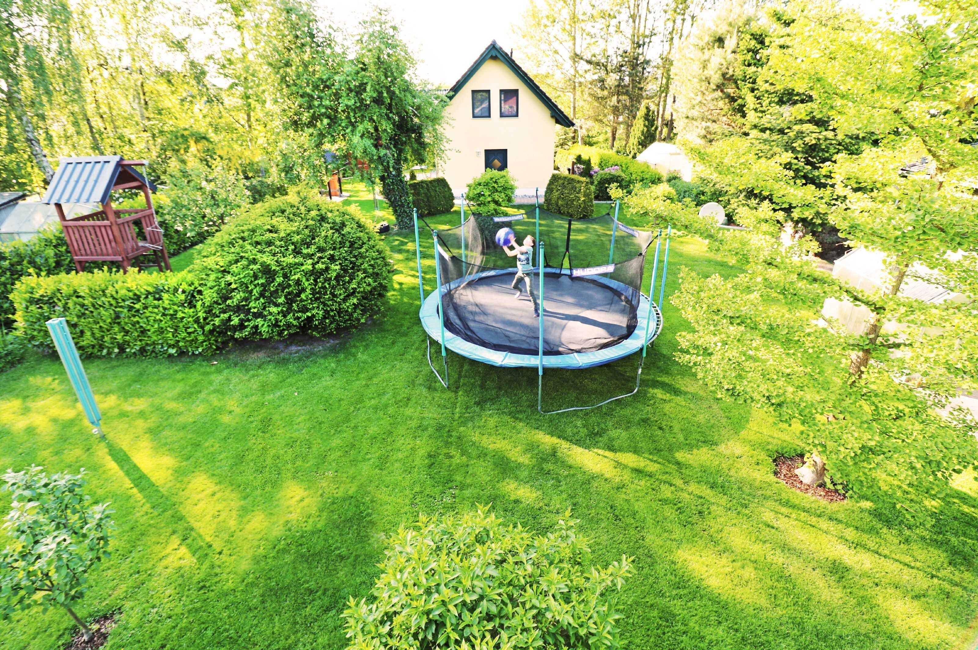 Ein Trampolin in einem gepflegten Garten, im Hintergrund ein Haus.