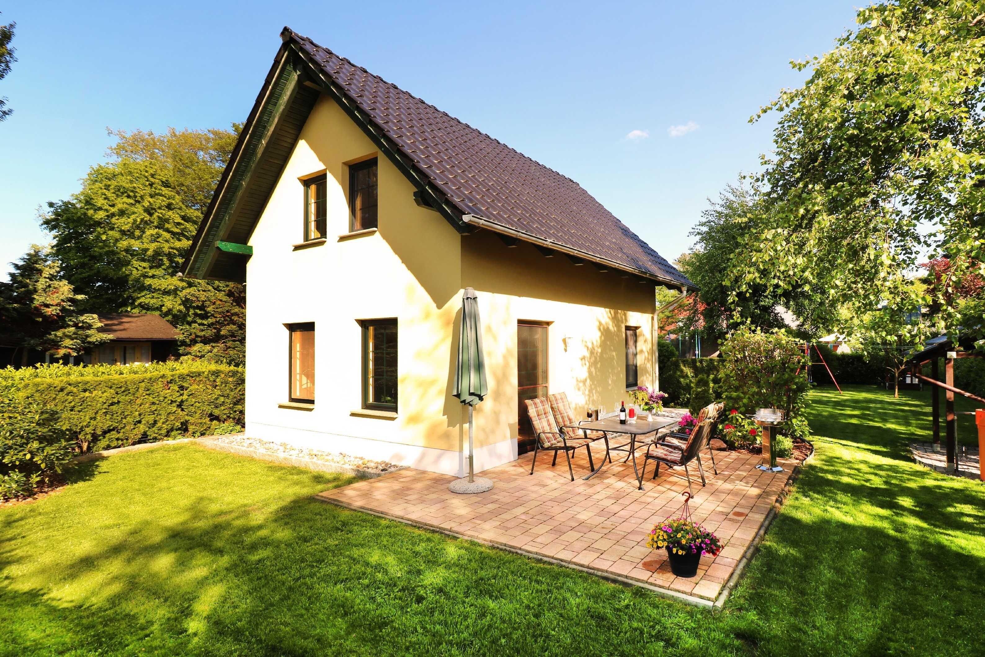 Ein zweistöckiges Haus mit geneigtem Dach, einer Terrasse mit Gartenmöbeln und einem gepflegten Garten.