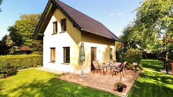 Ein zweistöckiges Haus mit geneigtem Dach, einer Terrasse mit Gartenmöbeln und einem gepflegten Garten.
