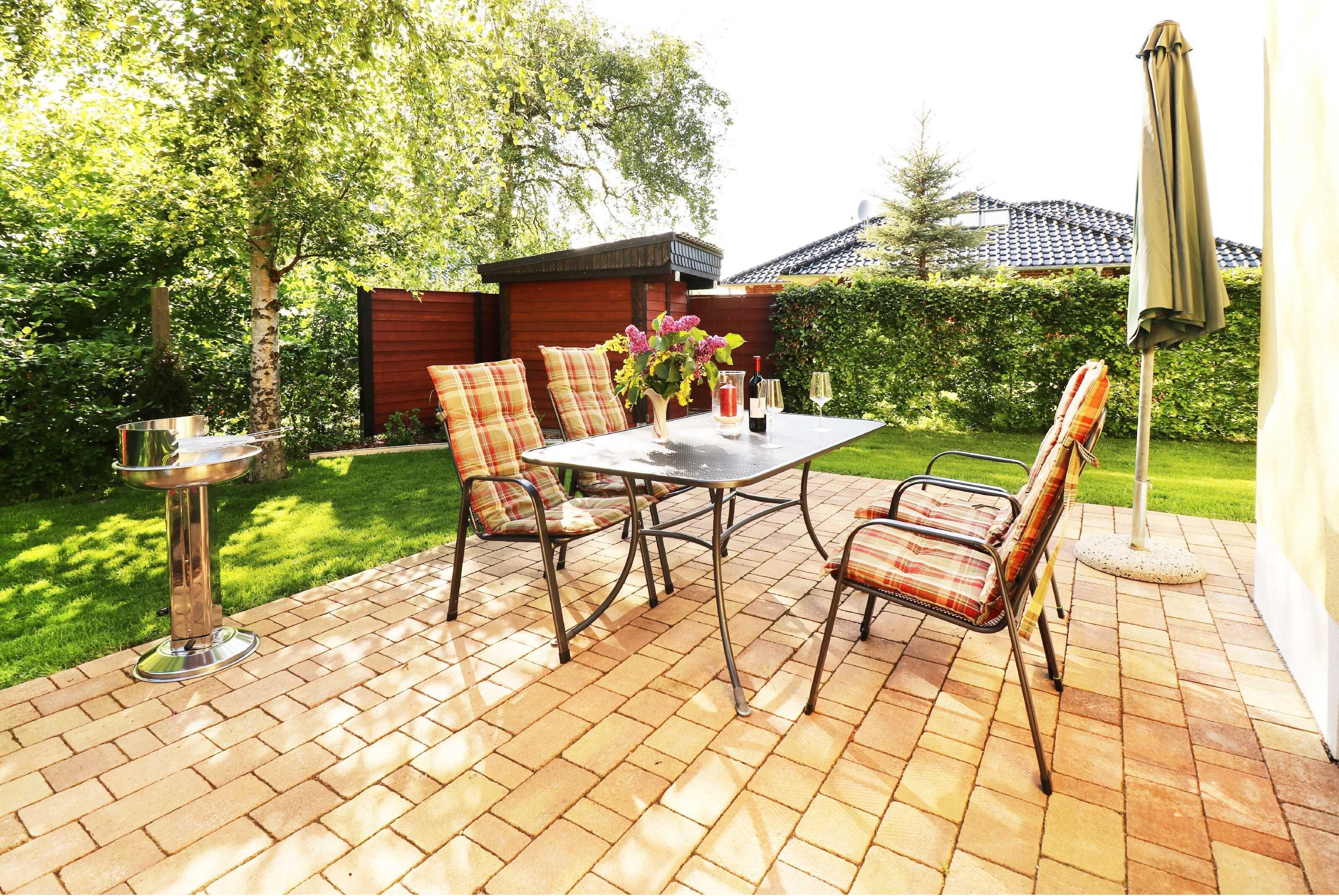 Eine Terrasse im Freien mit Tisch und Stühlen, einem Metallständer und einer kleinen Grünanlage.