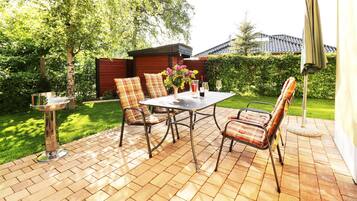 Eine Terrasse im Freien mit Tisch und Stühlen, einem Metallständer und einer kleinen Grünanlage.