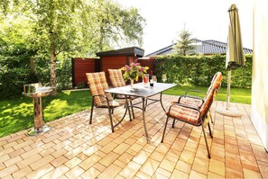 Eine Terrasse im Freien mit Tisch und Stühlen, einem Metallständer und einer kleinen Grünanlage.