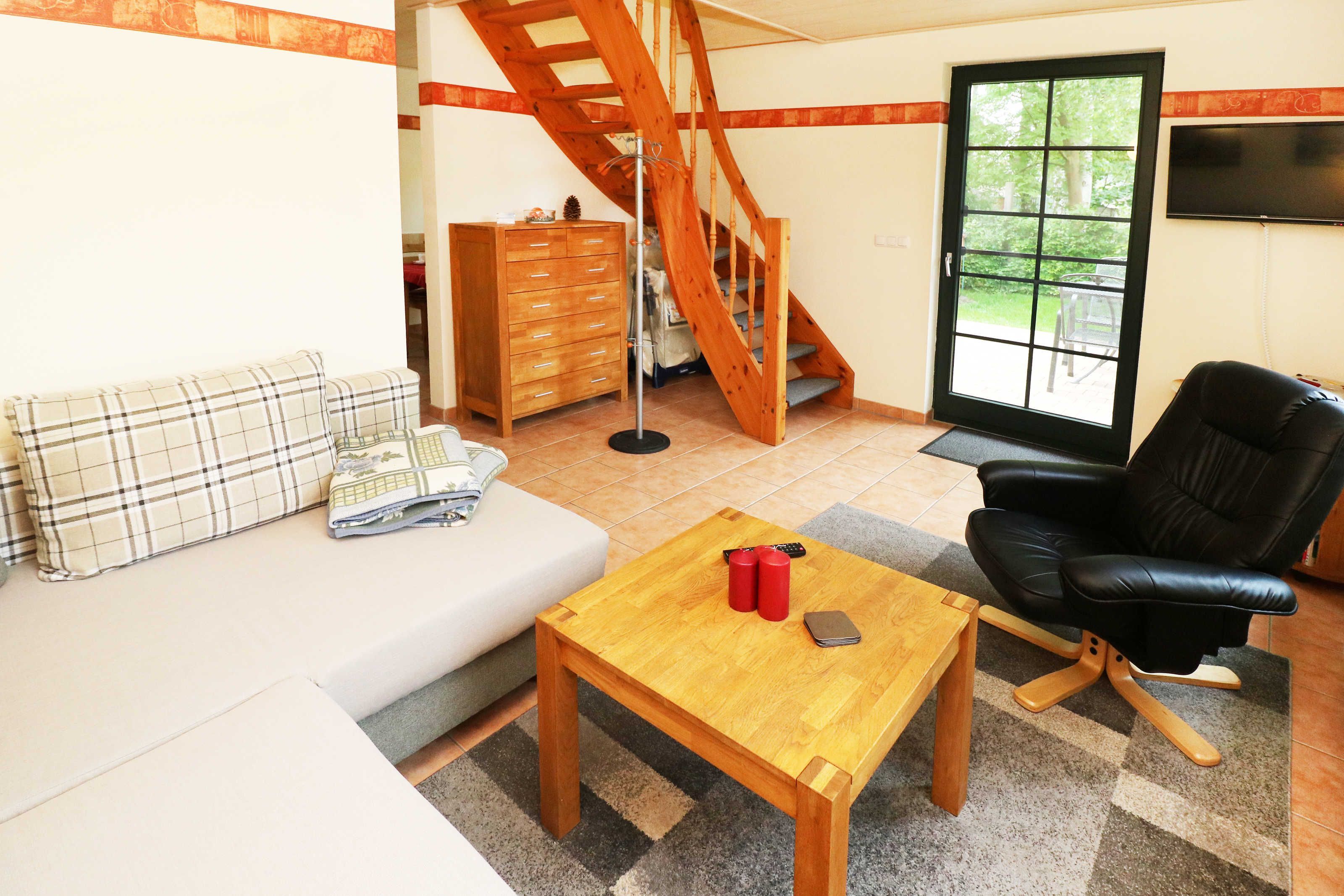 Ein Wohnzimmer mit einer Couch, einem Holztisch, einem schwarzen Ledersessel, einer Holzkommode, einer Treppe und einem an der Wand montierten Fernseher.