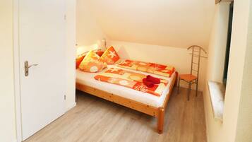 Ein kleines Zimmer mit einem Einzelbett, Holzboden, einer weißen Tür und einem kleinen Stuhl.