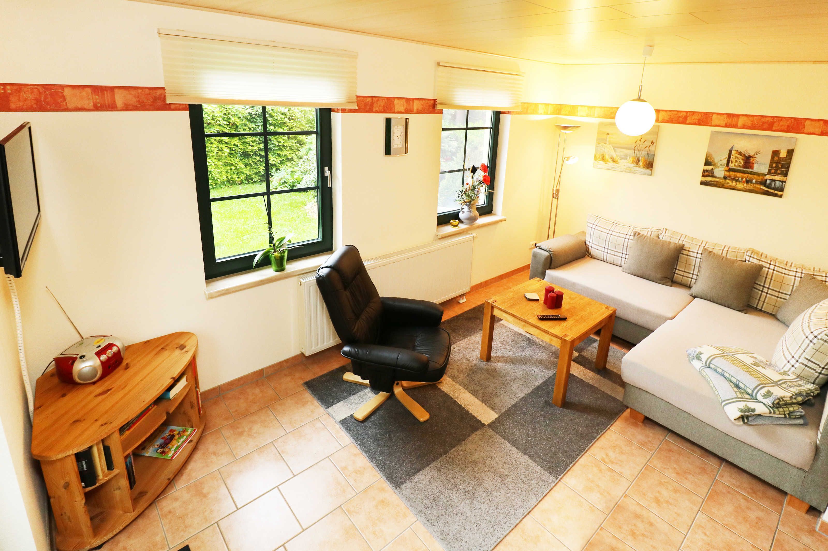 Ein gemütliches Wohnzimmer mit einer Couch, einem schwarzen Sessel, einem Holztisch und einer TV-Konsole mit einem Radio.