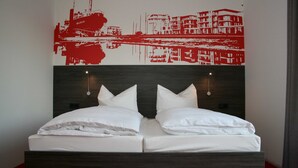 A double bed with white linens, a dark wood headboard, two wall-mounted lights, and a red and white cityscape artwork above. - Havenhostel Stade GmbH - Double room (Stade)