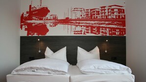A double bed with white linens, two bedside tables with lamps, and a red abstract artwork on the wall. - Havenhostel Stade GmbH - Double room (Stade)