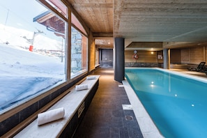 A pool area with a view of a snowy landscape, stone walls, and wooden beams.