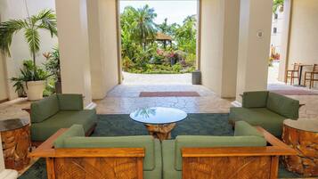 A lobby with green sofas, a central coffee table, and a view of a tropical garden.