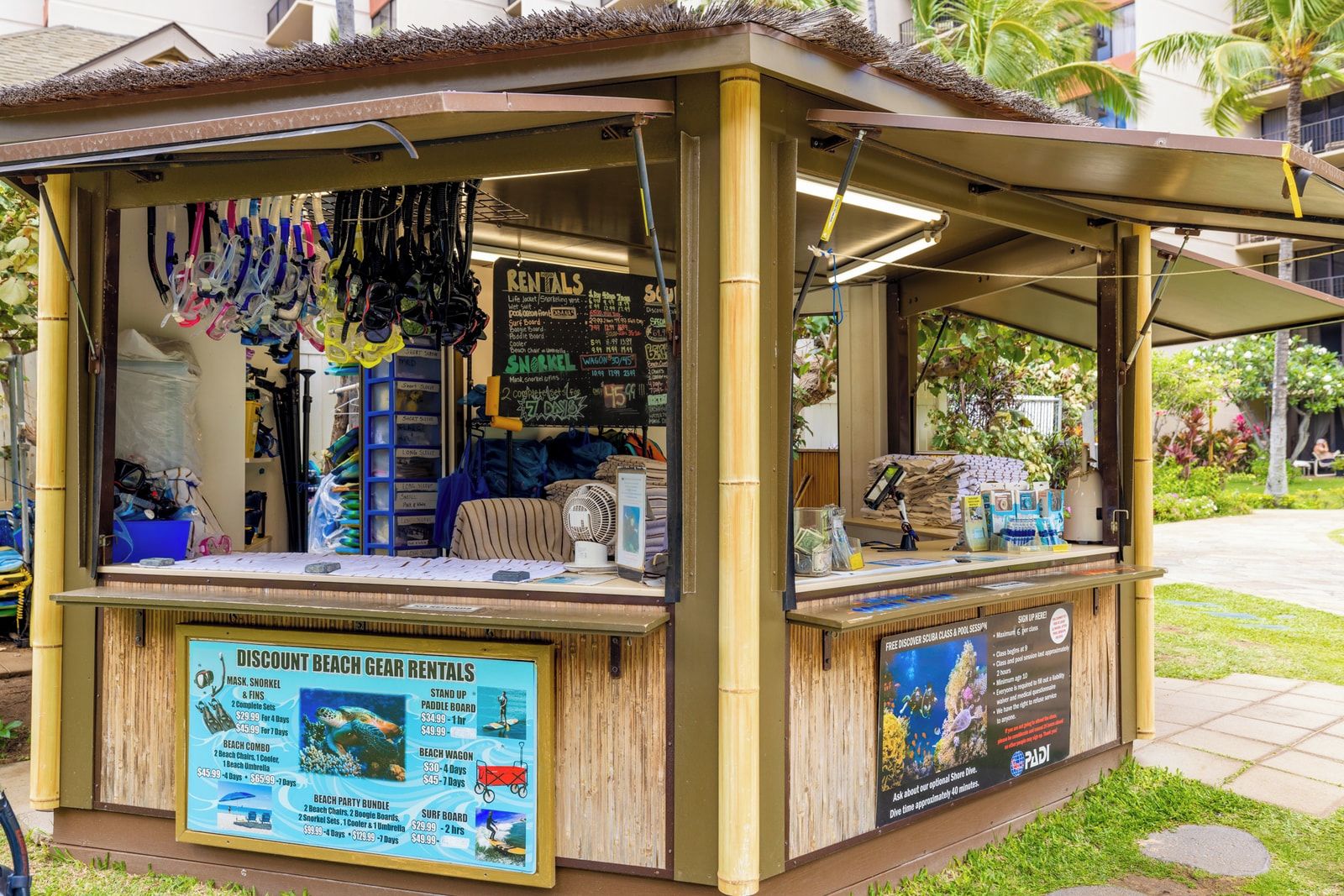 A beach gear rental kiosk with a sign listing items like snorkels, masks, and beach combos.