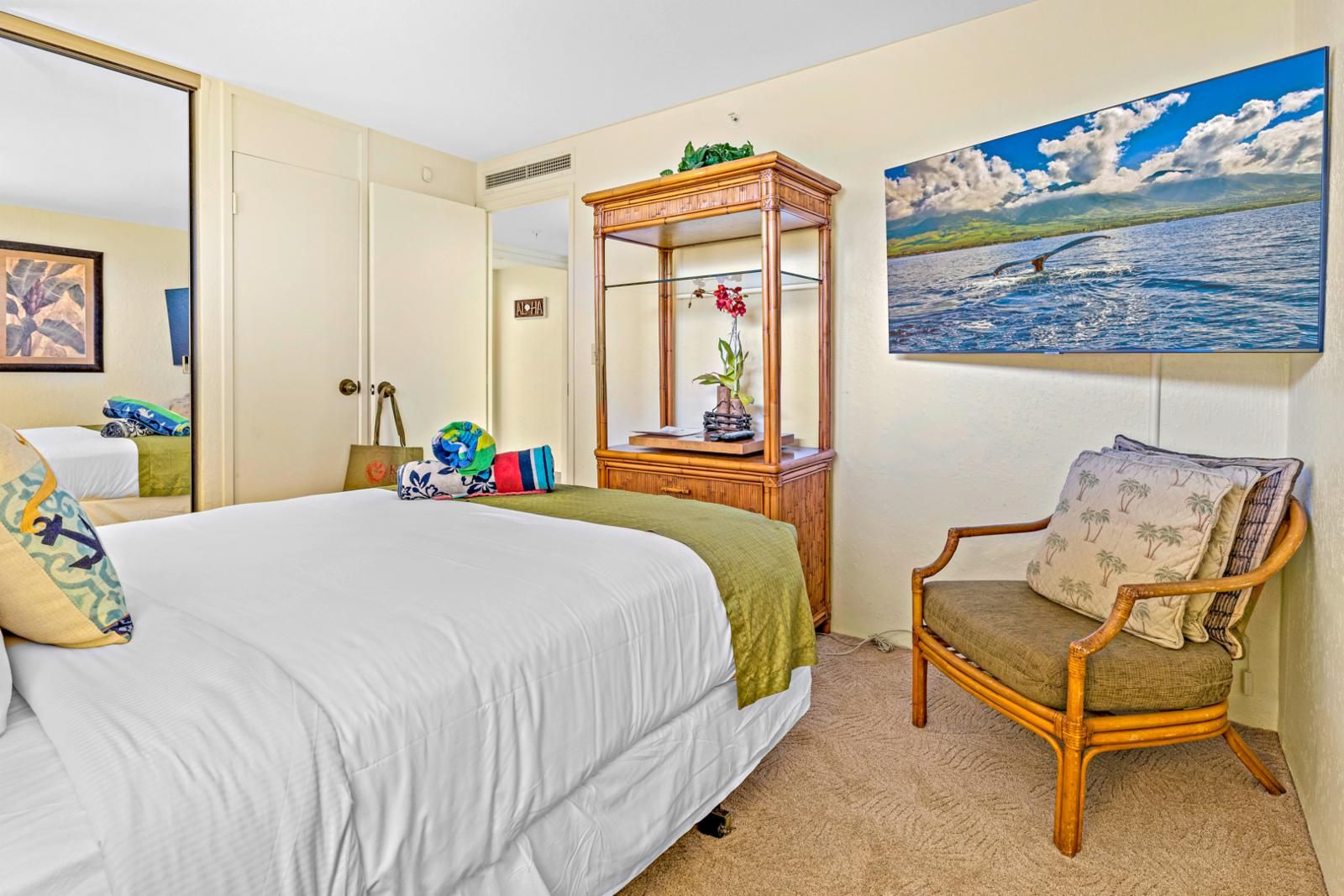 Una camera d'albergo con un letto grande, un comodino in legno, una poltrona con cuscini, uno specchio e un quadro raffigurante una scena marina.