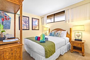 A hotel room with a four-poster bed, a wooden nightstand, a lamp, and framed artwork on the wall.