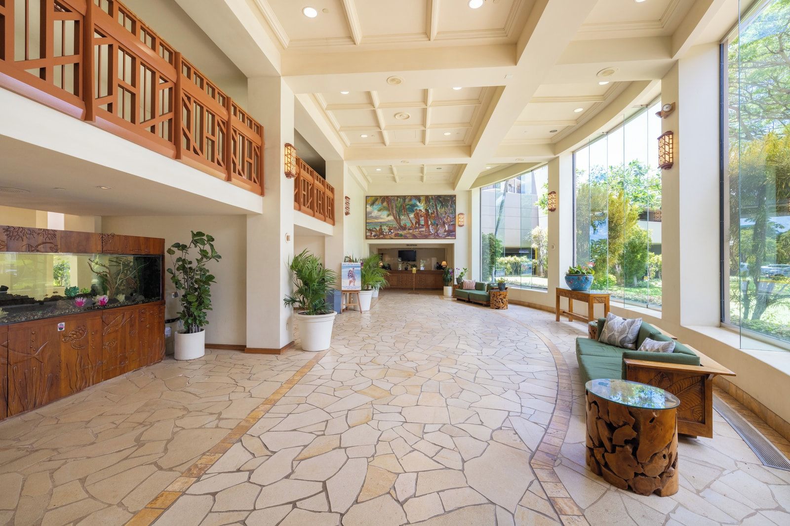 A spacious lobby with a large fish tank, potted plants, a reception desk, and a seating area with a view of the outdoors.