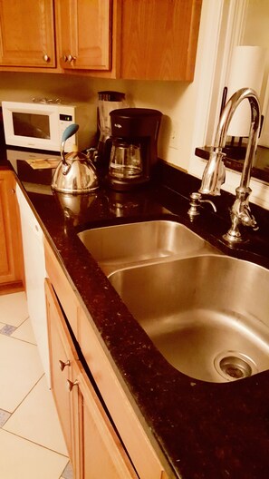 A kitchen with a stainless steel sink, a microwave, a coffee maker, and wooden cabinets. - Large bedroom (Orlando)