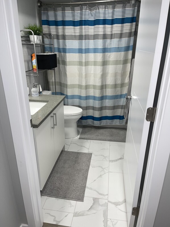 A bathroom with a toilet, a sink, a shower curtain, and a small rug.