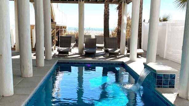 A rectangular pool with a waterfall feature, surrounded by white columns and lounge chairs. - ☆Oceanfront Serenity☆ Private Pool & Beach Walkway (Myrtle Beach)
