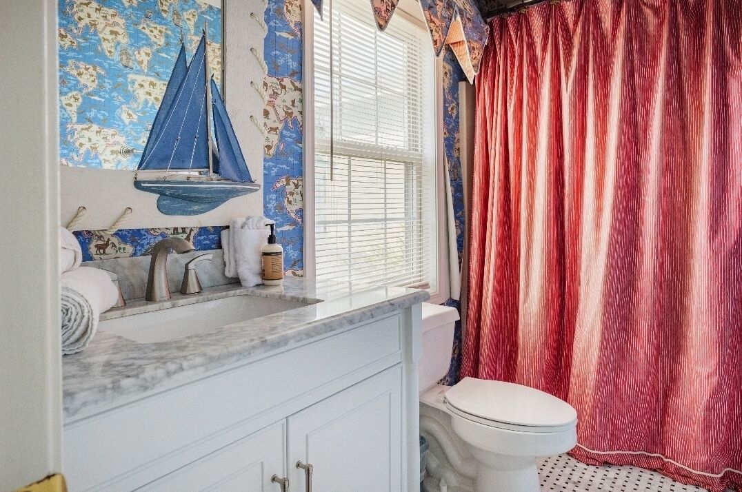 A bathroom with a nautical-themed wall, a white toilet, and a red curtain.